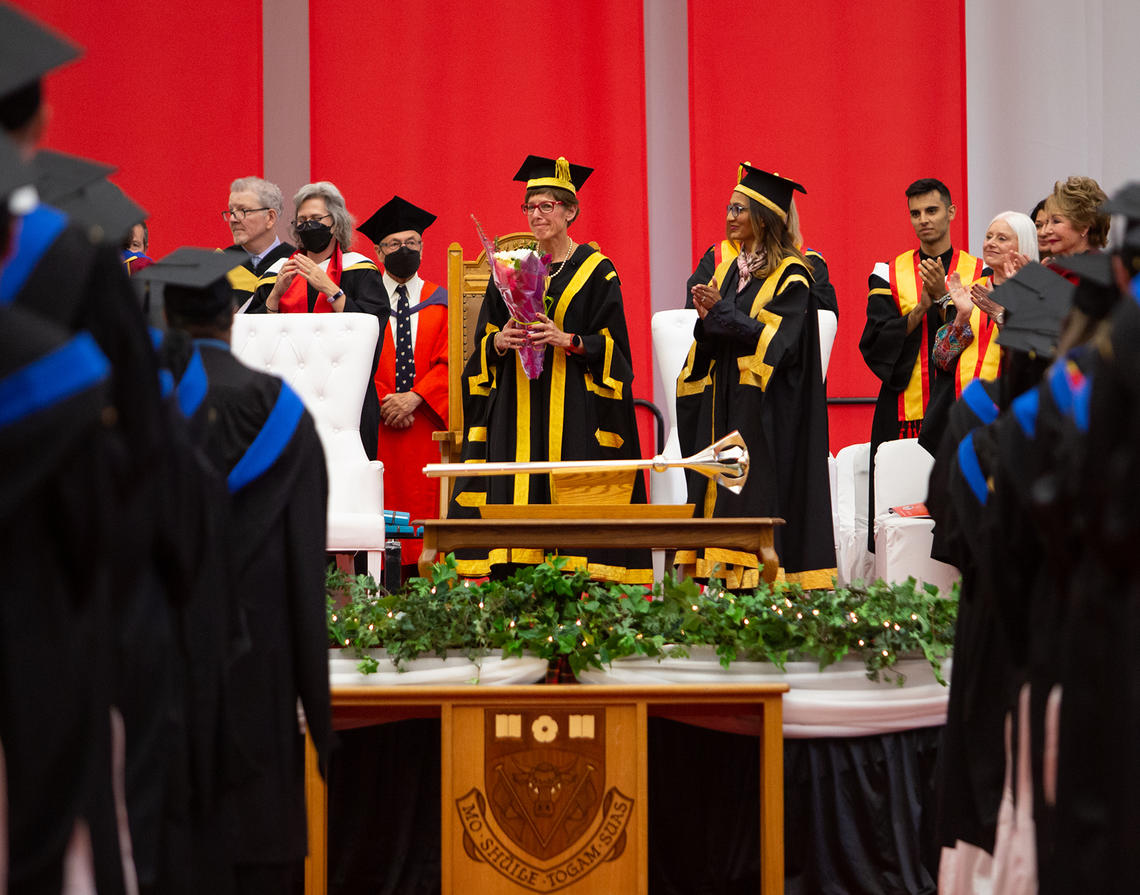 Chancellor Yedlin holds a bouquet of flowers on a stage as she was recognized for her service to the University during her final convocation ceremony on Friday, June 3. 
