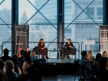 2025 PETRONAS Jackie Forrest and Anne Applebaum conversing on the stage from a far angle and guests in frame